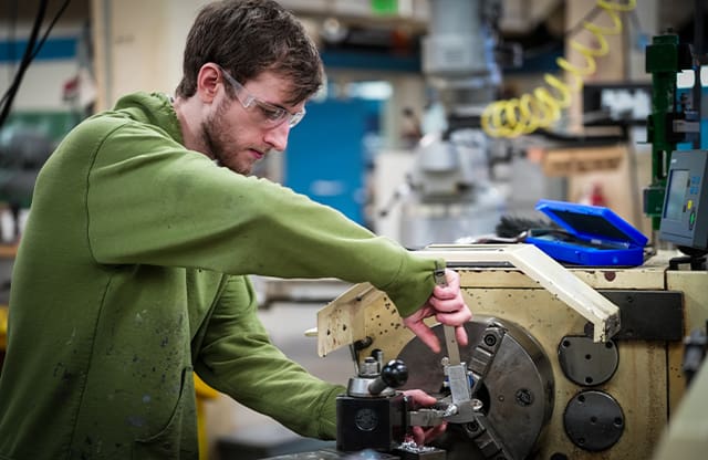 A Manufacturing Academy student uses a caliper to measure his part in the machine shop.