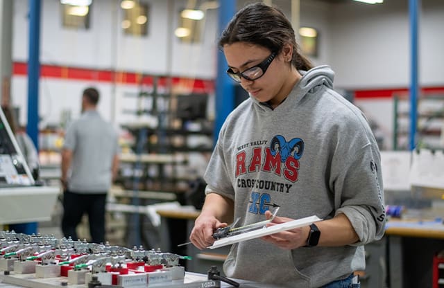 An AJAC Apprentice uses a caliper to measure a part on the shop floor during his apprenticeship.